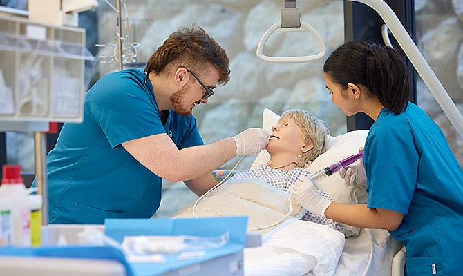Zwei Studierende in blauen Shirts üben an einer Puppe