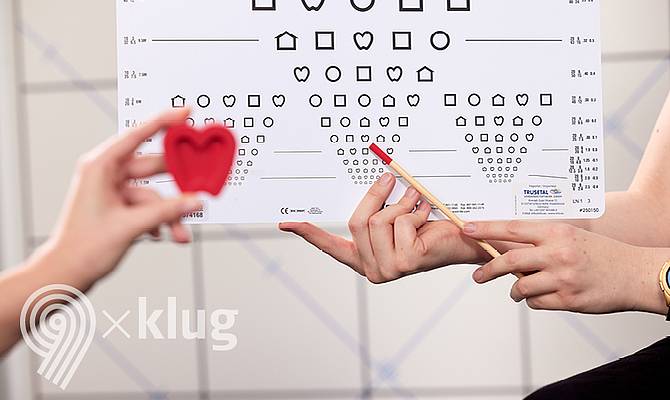 Sehtesttafel im Hintergrund und eine Hand die ein rotes Herz davor hält 