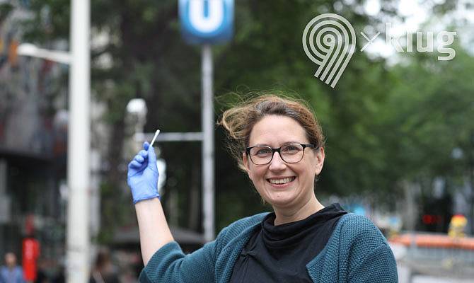 Frau mit Wattestäbchen vor einer U-Bahn-Station stehend 