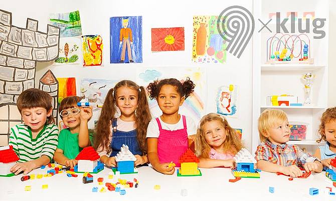 Kinder sitzen aufgereiht an einem Tisch mit buntem Bastelmaterial