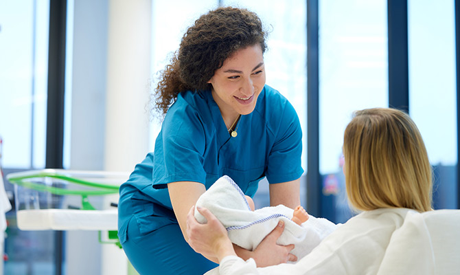 Studierende übergibt Säuglingspuppe einer Dame im Krankenbett