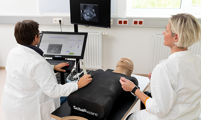 Zwei Menschen sitzen untersuchen eine Puppe mittels Sonographiegerätes