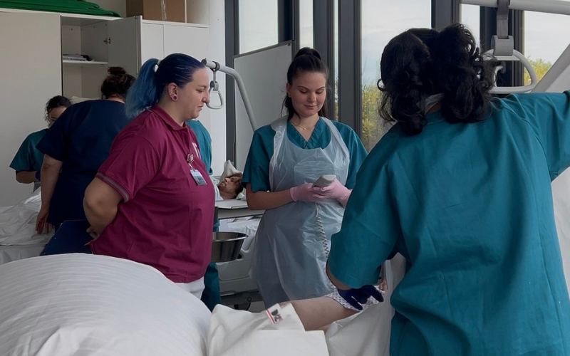 Gesundheits- undKrankenpflege-Studierenden stehen mit einer Praxisanleiterin vor einem Bett mit einem/einer Patienten/Patientin