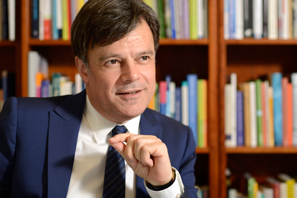 Giovanni Maio in Anzug mit Krawatte sitzt vor Bücherregal