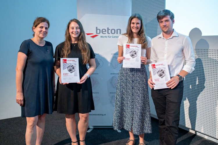 Vier Personen stehen nebeneinander auf einer Bühne vor einem Roll-up von Beton Dialog Österreich. Drei von ihnen halten Urkunden der Concrete Design Competition in den Händen und blicken lächelnd in die Kamera. Die Gruppe trägt sommerliche, schlichte Kleidung und posiert für ein Erinnerungsfoto der Preisverleihung.