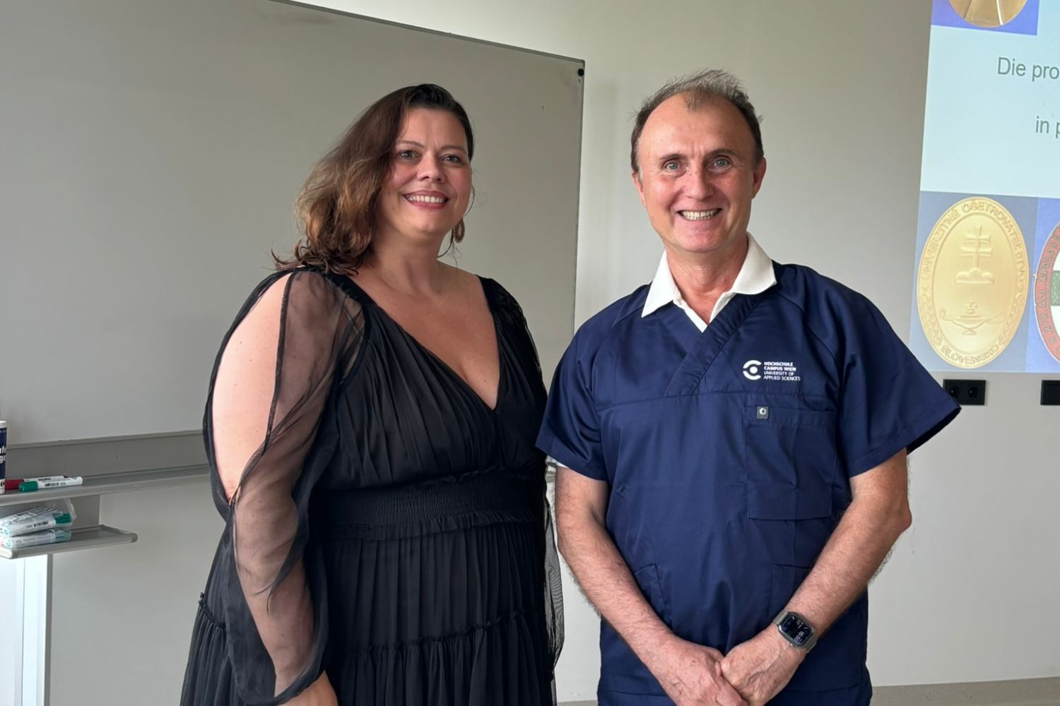 Eine Frau und ein Mann vor einer Präsentation, auf der Orden und Broschen zu sehen sind