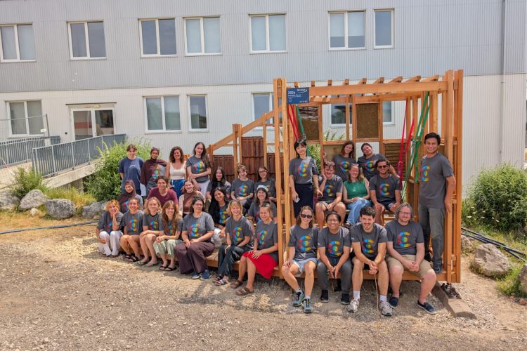 Gruppenfoto von rund 30 Teilnehmenden vor einer selbst gebauten Holzkonstruktion im Freien.